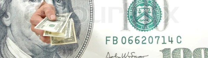 Hand holding hundred dollar bills through a large hundred dollar bill